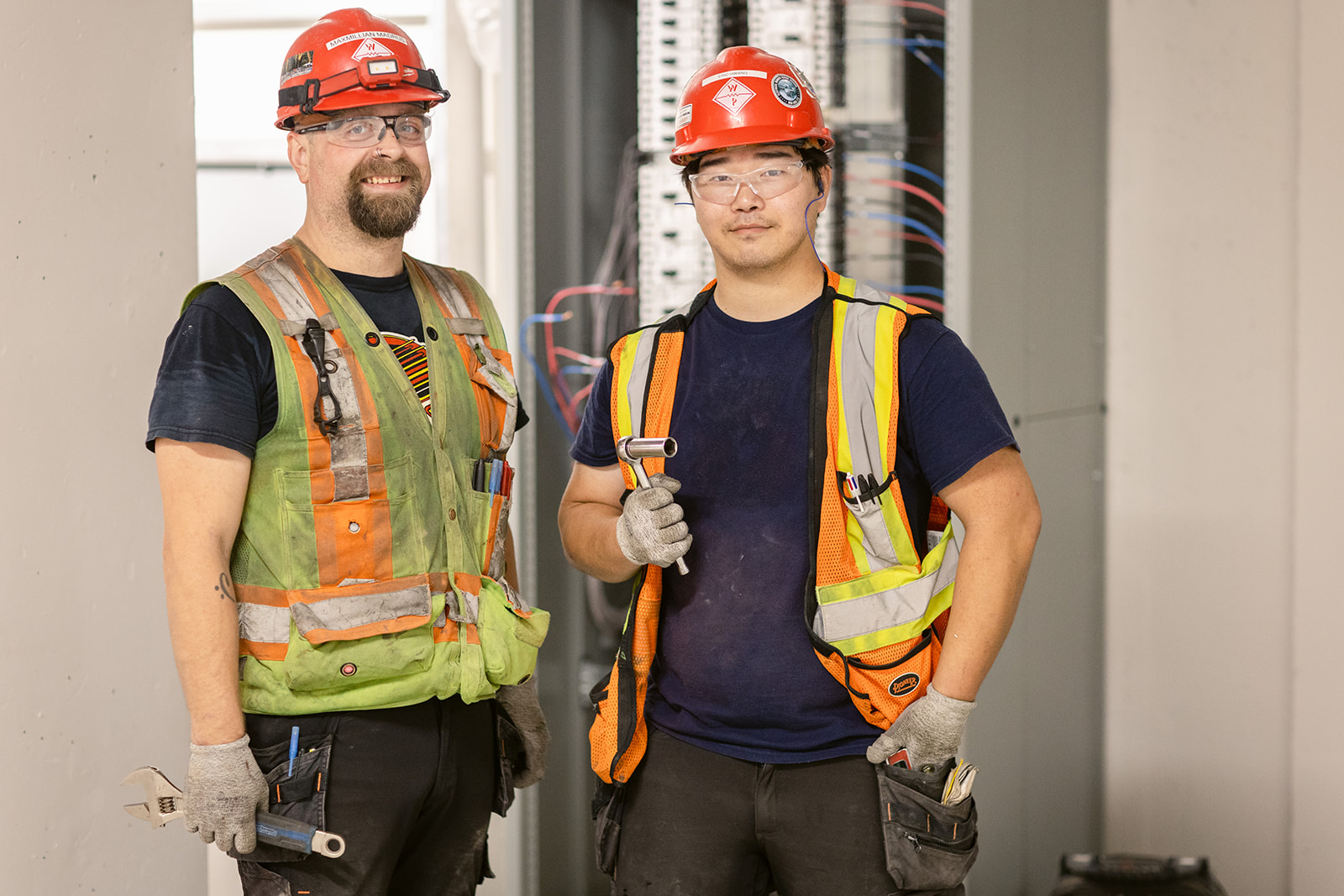 Two tradespeople in PPE on the jobsite, holding tools. 