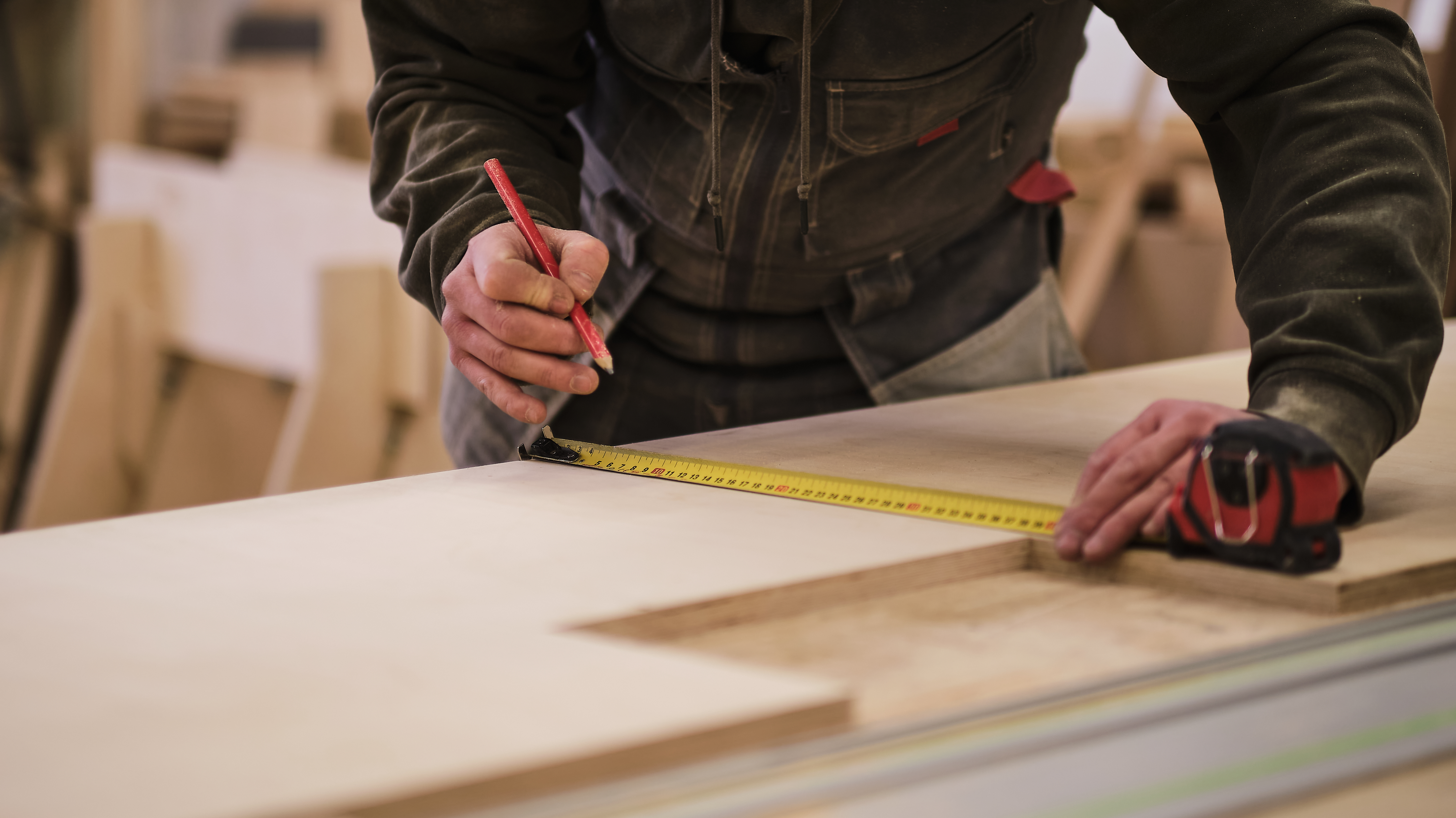 person measuring wood with measuring tape and pencil