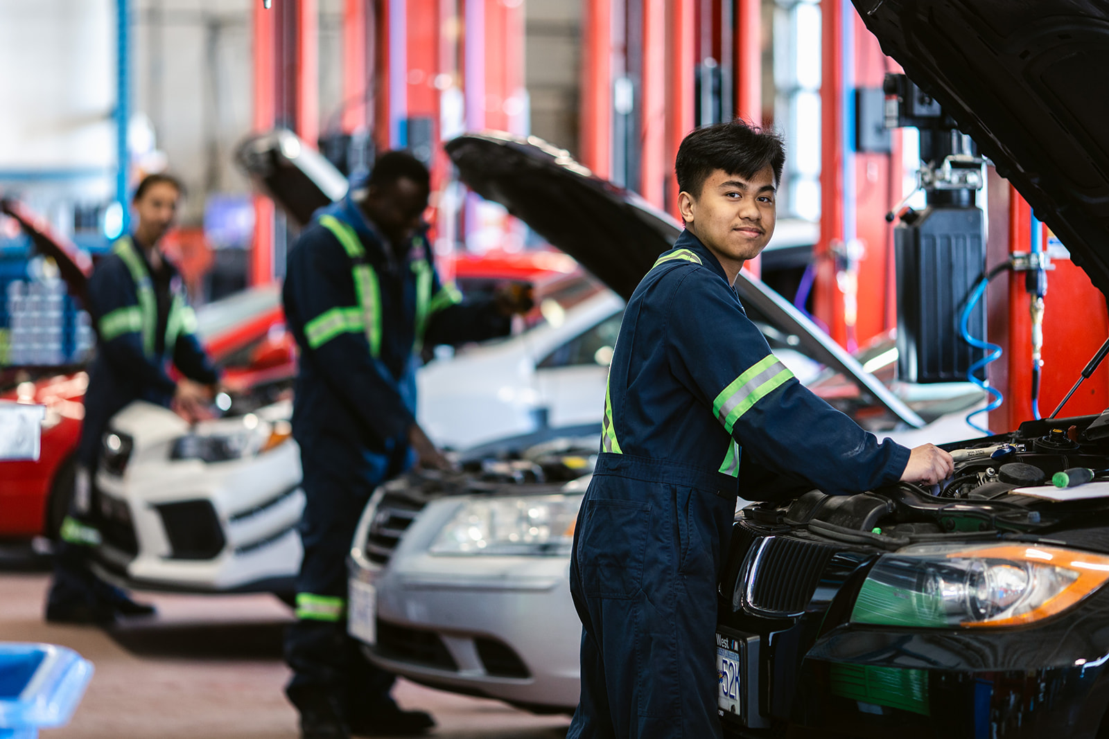 Automotive Service Technicians in garage working on hood of cars