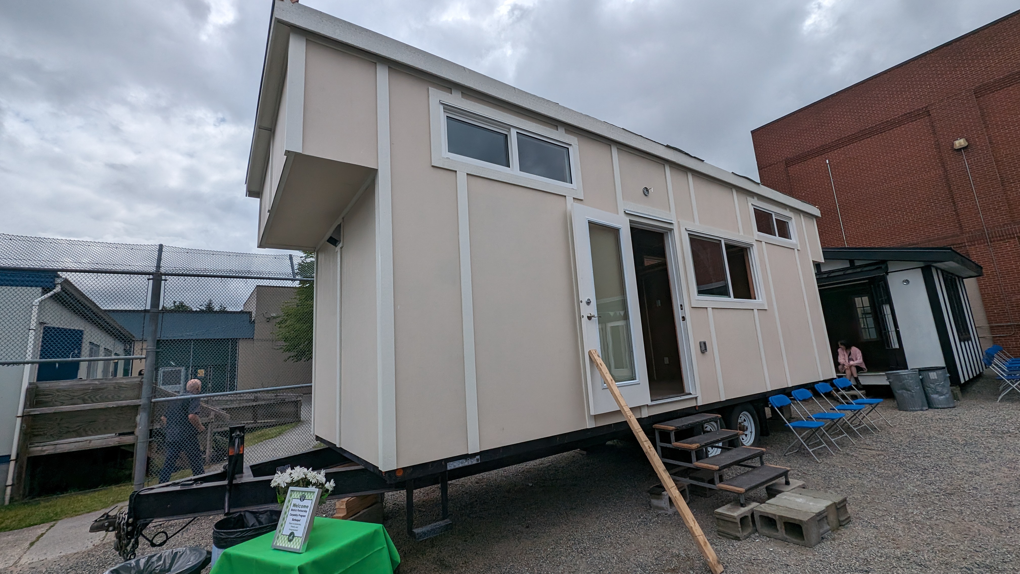 Tiny home on trailer. Beige. Stairs leading up to an open door. Three sets of windows looking out.