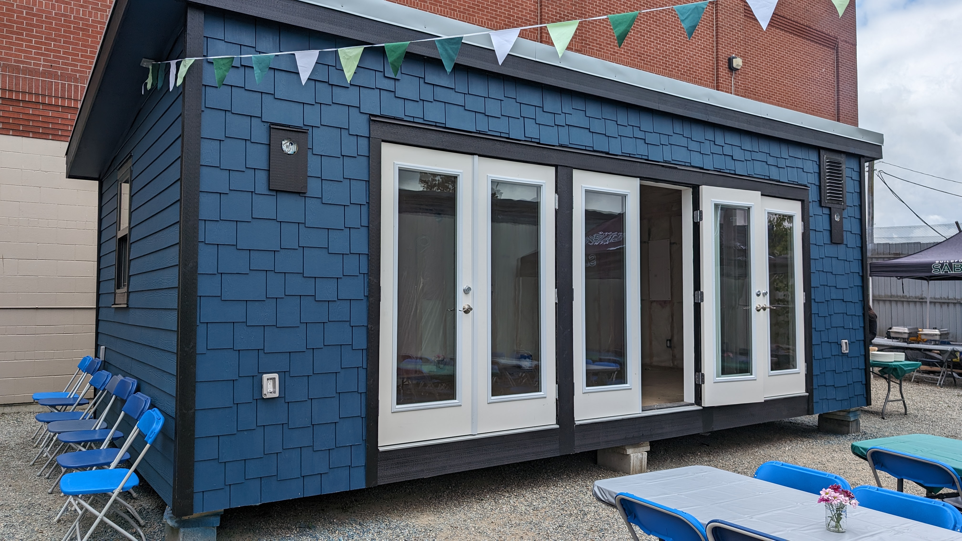 Tiny house with blue shingles and three sets of double doors. The middle doors are open, inviting you to take a peak inside.,